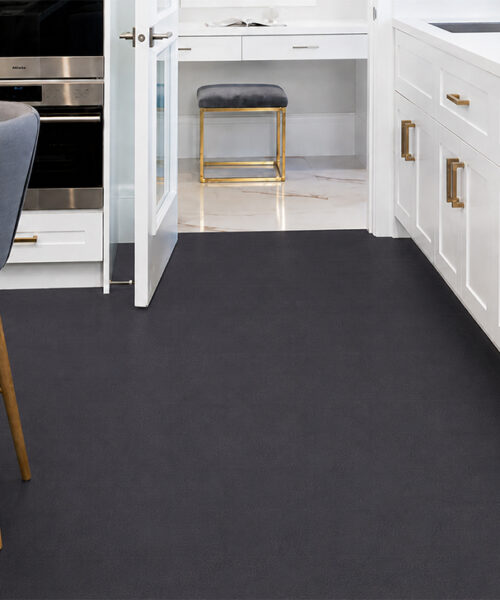 Rich black leather plank flooring in a bright white kitchen with marble counters, gray stools and brushed brass cabinet hardware.