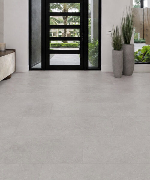 Bright Stone click-lock flooring creates a seamless pale gray surface in a modern entryway with a wood console and glass shower enclosure.