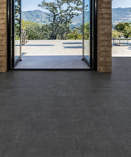 Concrete Alloy dark gray flooring throughout a luxury open-plan living room with marble walls and glass windows.