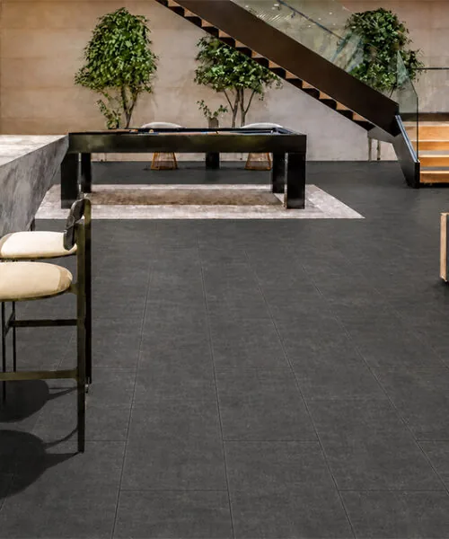 Concrete Alloy dark gray TechSlate flooring in an open-plan game room with a home bar and staircase.