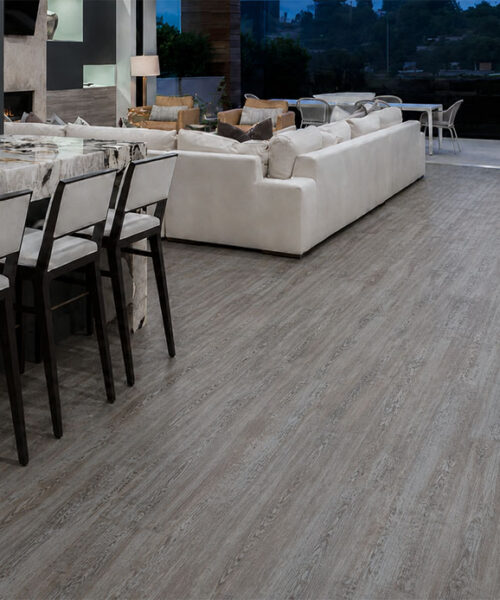 Earthy Pine wood-look natural composite flooring runs through an open dining and lounge space with pale seating.