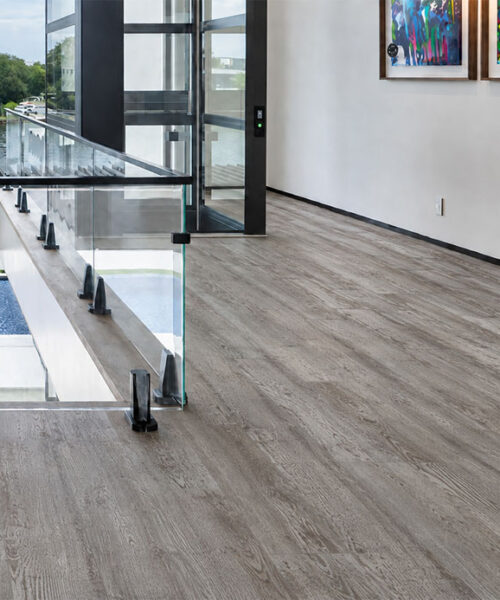 Earthy Pine natural composite click-lock flooring brings muted gray wood grain to a bright gallery corridor.