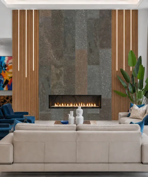 Modern fireplace wall clad in Gold Mica Slate stone tiles with natural variation and elegant vertical wood accents