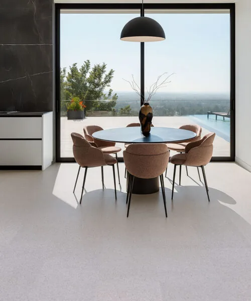Grano - 25/64" (10mm) - Cork Floating (FGra10) Bright dining area with floor-to-ceiling windows, elegant beige chairs, and warm Grano cork flooring that enhances the natural light and open feel.