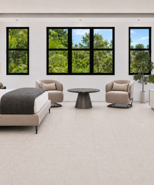 Matera Blend -19/64" (7.5mm) - Swiss Techslate (MMatBd7.5) Light limestone Matera Blend TechSlate flooring forms a subtle stone-look rectangular plank layout in a bedroom with upholstered bed and armchairs.