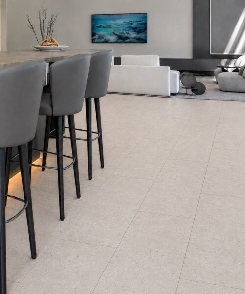 Matera Blend -19/64" (7.5mm) - Swiss Techslate (MMatBd7.5) Light limestone Matera Blend stone-look flooring extends across a kitchen and living area beneath a wood island with bar stools.