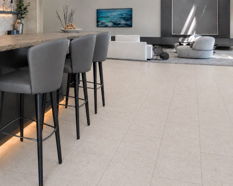 Light limestone Matera Blend stone-look flooring extends across a kitchen and living area beneath a wood island with bar stools.