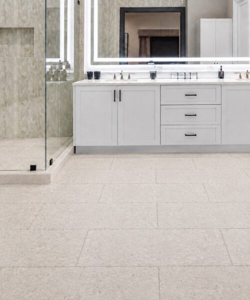 Matera Blend -19/64" (7.5mm) - Swiss Techslate (MMatBd7.5) Matera Blend mineral-based flooring in light limestone covers a bathroom floor with rectangular planks, glass shower enclosure, and white vanity.