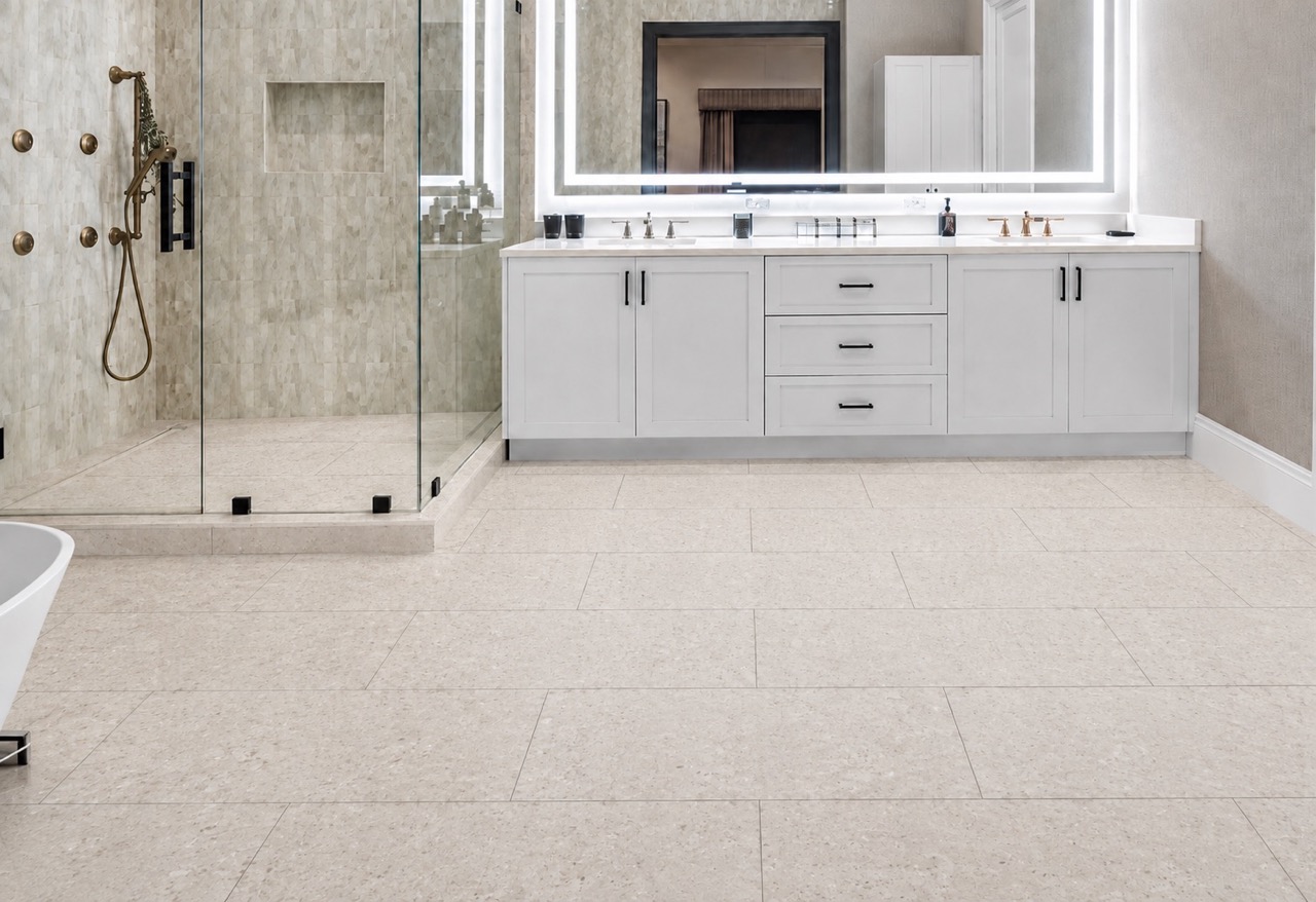 Matera Blend -19/64" (7.5mm) - Swiss Techslate (MMatBd7.5) Matera Blend mineral-based flooring in light limestone covers a bathroom floor with rectangular planks, glass shower enclosure, and white vanity.