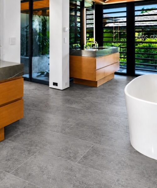 Midnight Slate Swiss TechSlate flooring shows a gray, mottled slate-look mineral surface in a modern bathroom with a freestanding tub and wood vanity.