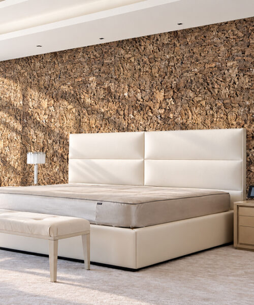Roccia 28mm natural brown textured cork wall panels installed as a floor-to-ceiling bedroom accent wall behind a white upholstered bed in a luxury master bedroom. Copy