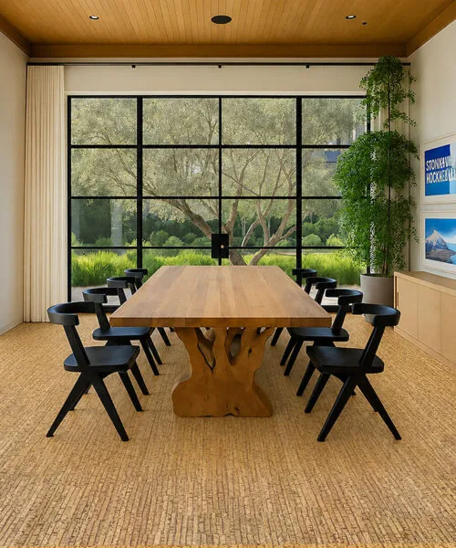 Sisal cork flooring in a spacious dining room featuring a large natural wood table, black chairs, and floor-to-ceiling garden views.