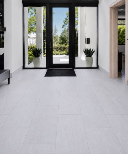 Snowstone light gray mineral-based flooring forms a staggered plank layout in a modern entryway with black-framed glass doors.