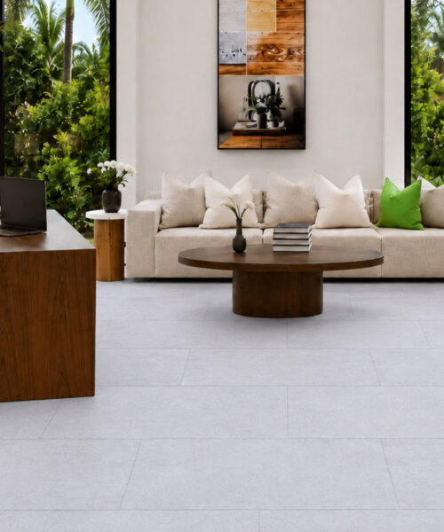 Snowstone light gray TechSlate flooring creates a home office with a wood desk, sofa, greenery, and large windows.
