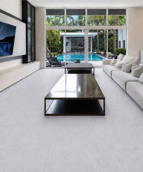 Snowstone large-format stone-look flooring spans a bright living room with white sofas, a black coffee table, and pool views.