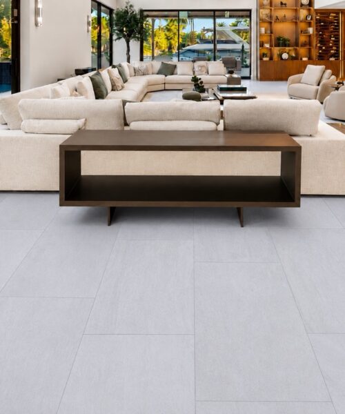 Snowstone light gray TechSlate flooring fills a spacious living room with sectional seating, dark wood furniture, and pool views.