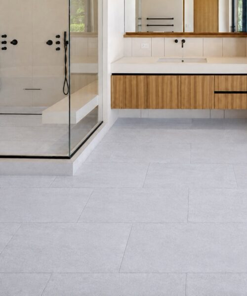 Snowstone waterproof floating flooring shows a light gray concrete-look pattern across a modern bathroom with a glass shower.