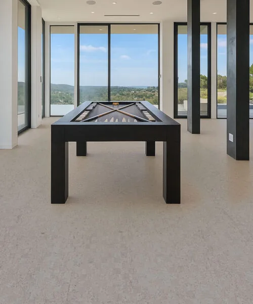 Modern game room with pool table on light gray cork flooring, large windows, and panoramic outdoor views