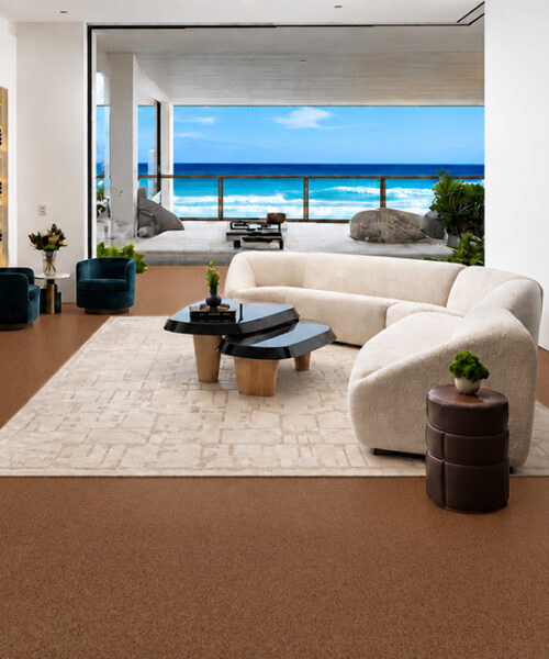 Venetian - 25/64" (10mm) - Cork Floating (FVen10) Reddish-brown Venetian natural cork flooring frames a curved cream sectional in an oceanfront living room.