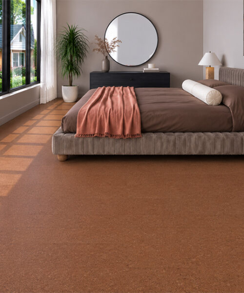 Venetian - 25/64" (10mm) - Cork Floating (FVen10) Venetian 10mm comfortable cork flooring with reddish-brown speckling surrounds an upholstered bed and dark nightstands.